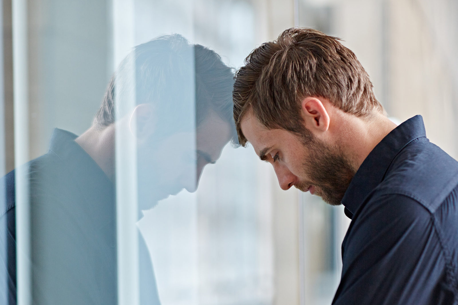 Man with head against a window feeling anxious