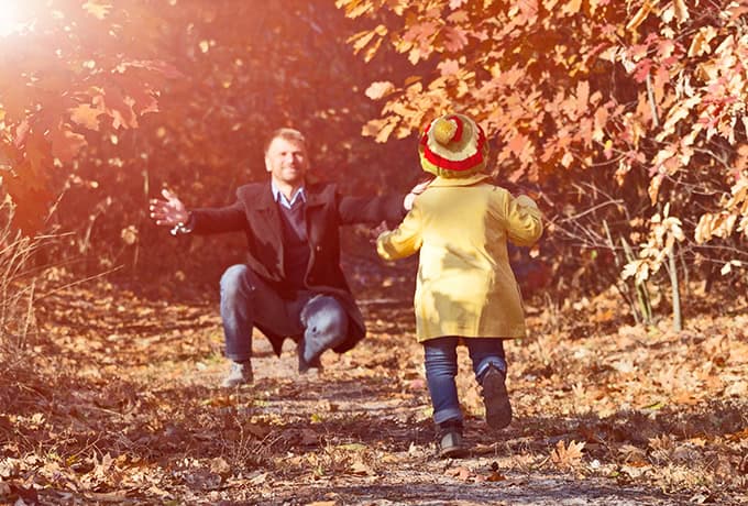 Child running towards father in forest.