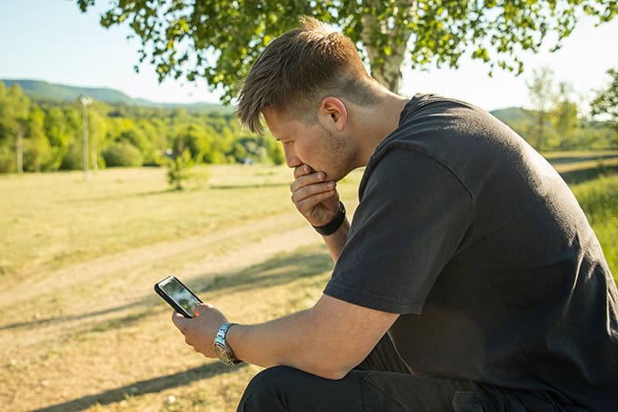 Man sitting alone outside thinking and looking at phone