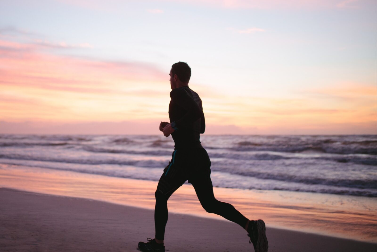 Silhouette of man running along the beach at sunrise